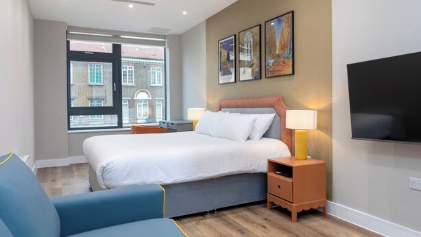 Une chambre d’hôtel moderne, dotée d’un grand lit, d’un bureau, d’une chaise, d’une télévision et d’œuvres d’art accrochées au mur.
