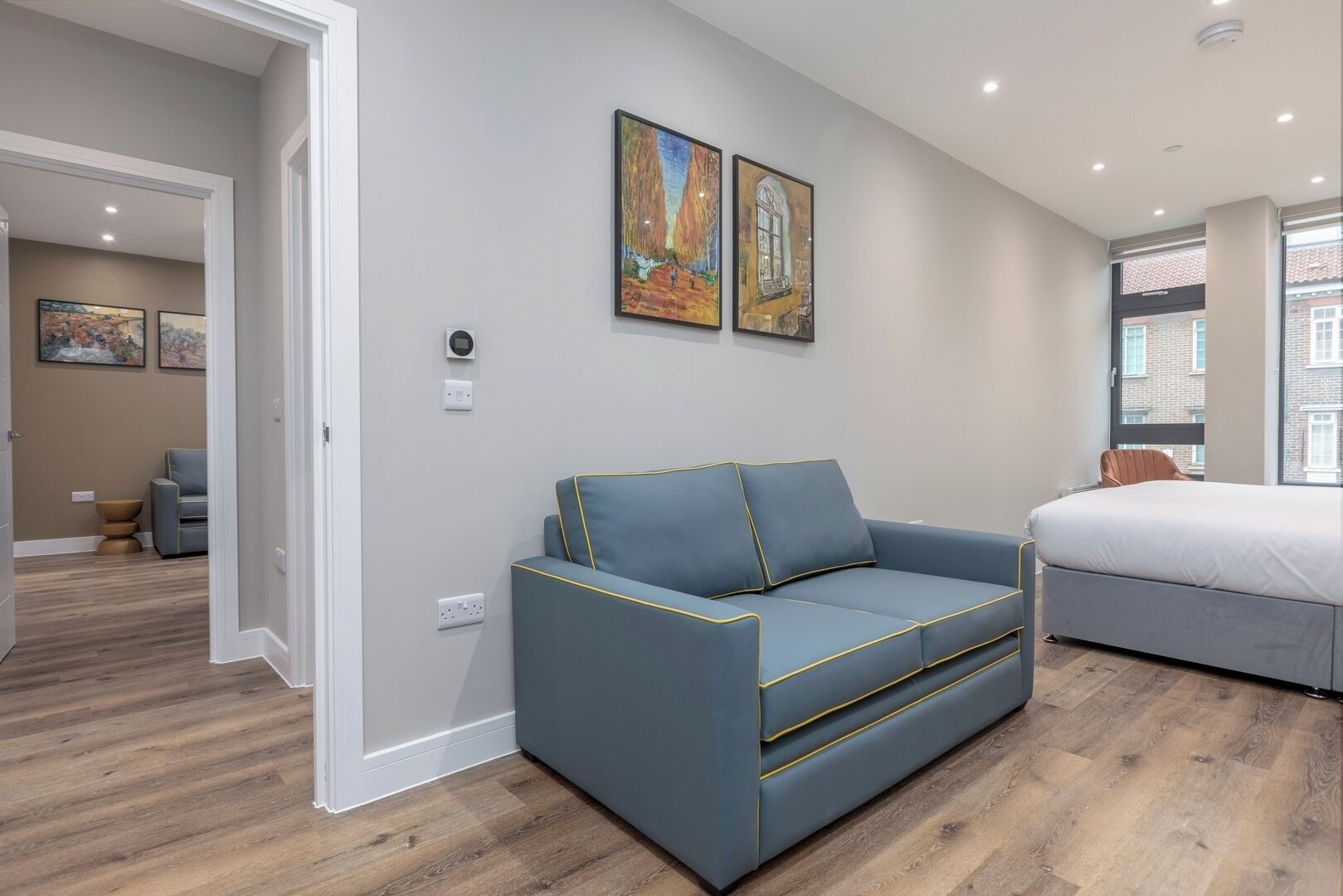Un dormitorio moderno con un sofá azul, una cama y dos cuadros en la pared.