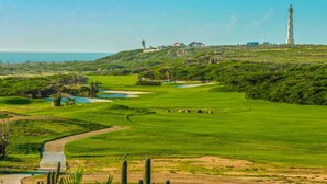 Un campo de golf con búnkeres, un estanque y un faro a lo lejos.