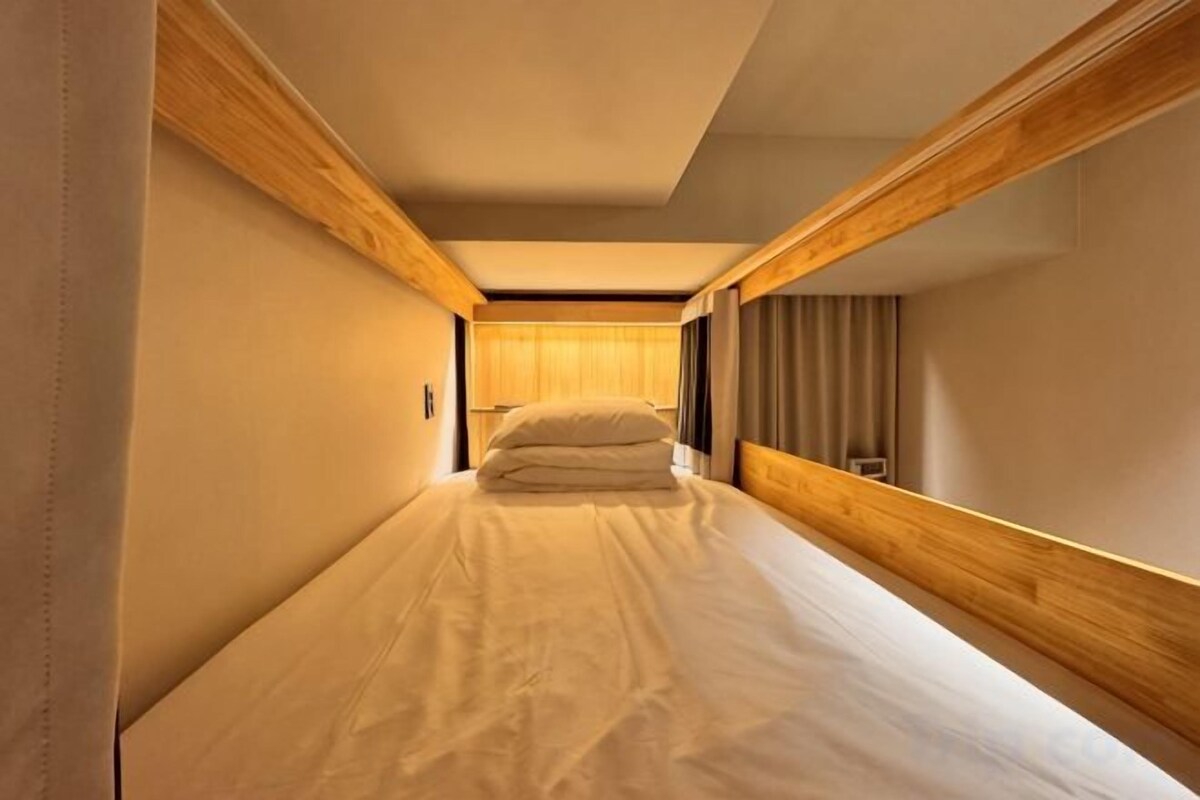 Een kleine kamer met een enkel bed, houten hoofdbord en zijwanden, een nachtkastje en een lamp.