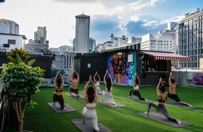 A rooftop yoga class with participants on mats, surrounded by city buildings and a graffiti wall.