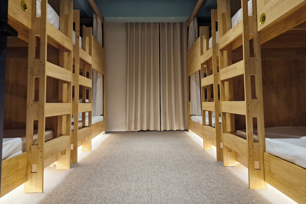 Een kamer met stapelbedden die in een U-vorm zijn gerangschikt, een vloerkleed en een gordijn op de achtergrond.