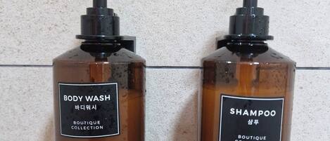 To flasker bodywash og shampoo med sorte pumper, mærket både på engelsk og koreansk, foran en struktureret væg.