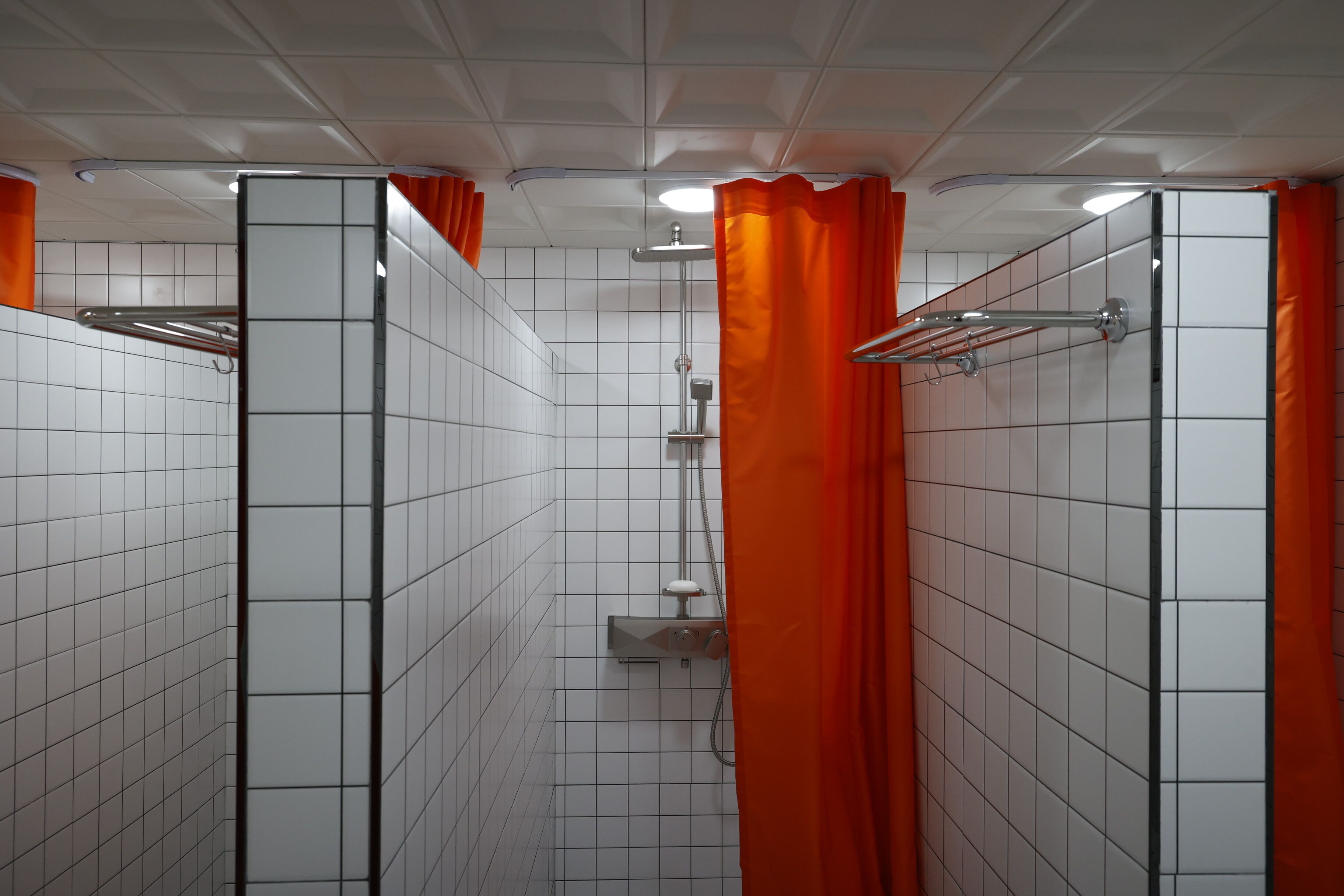 A tiled bathroom with a shower, orange curtains, and a mirror.