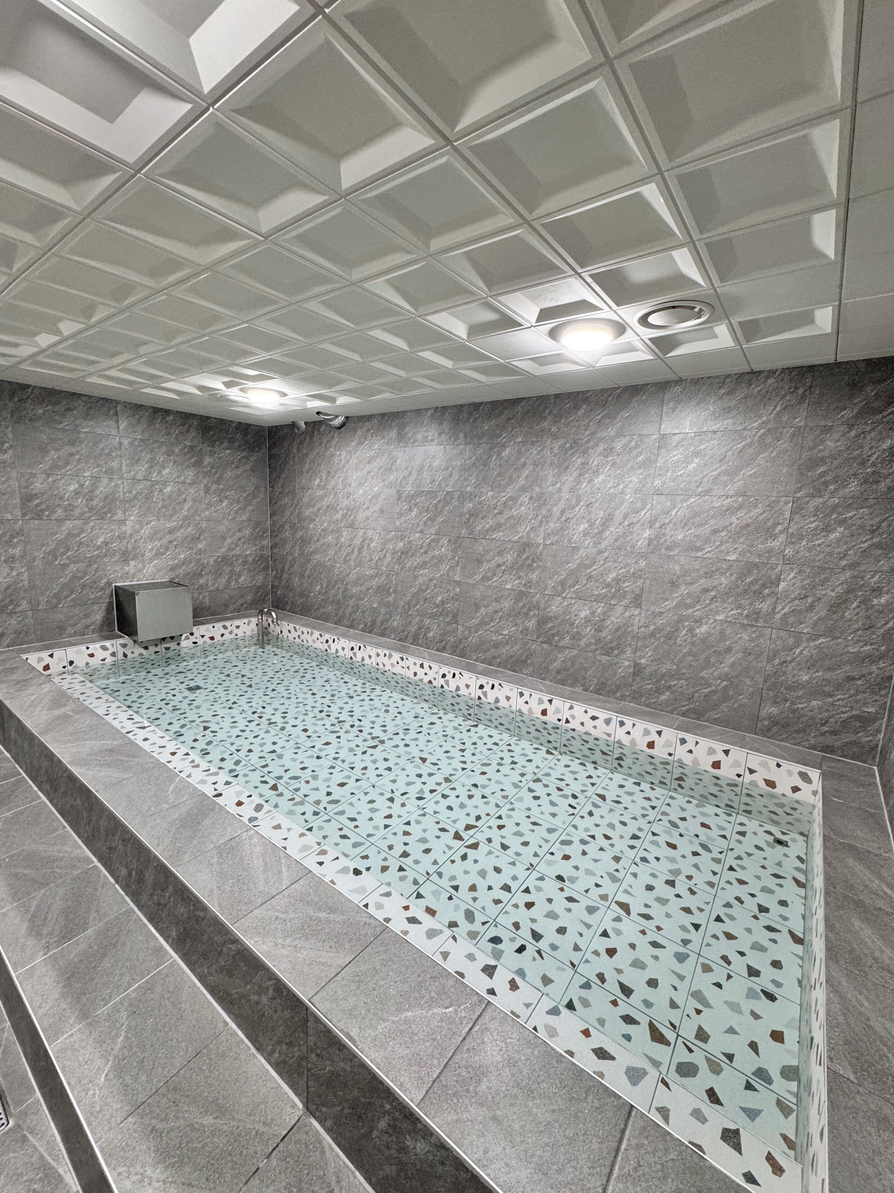 A modern bathroom with a large bathtub, grey marble walls, and a patterned floor.