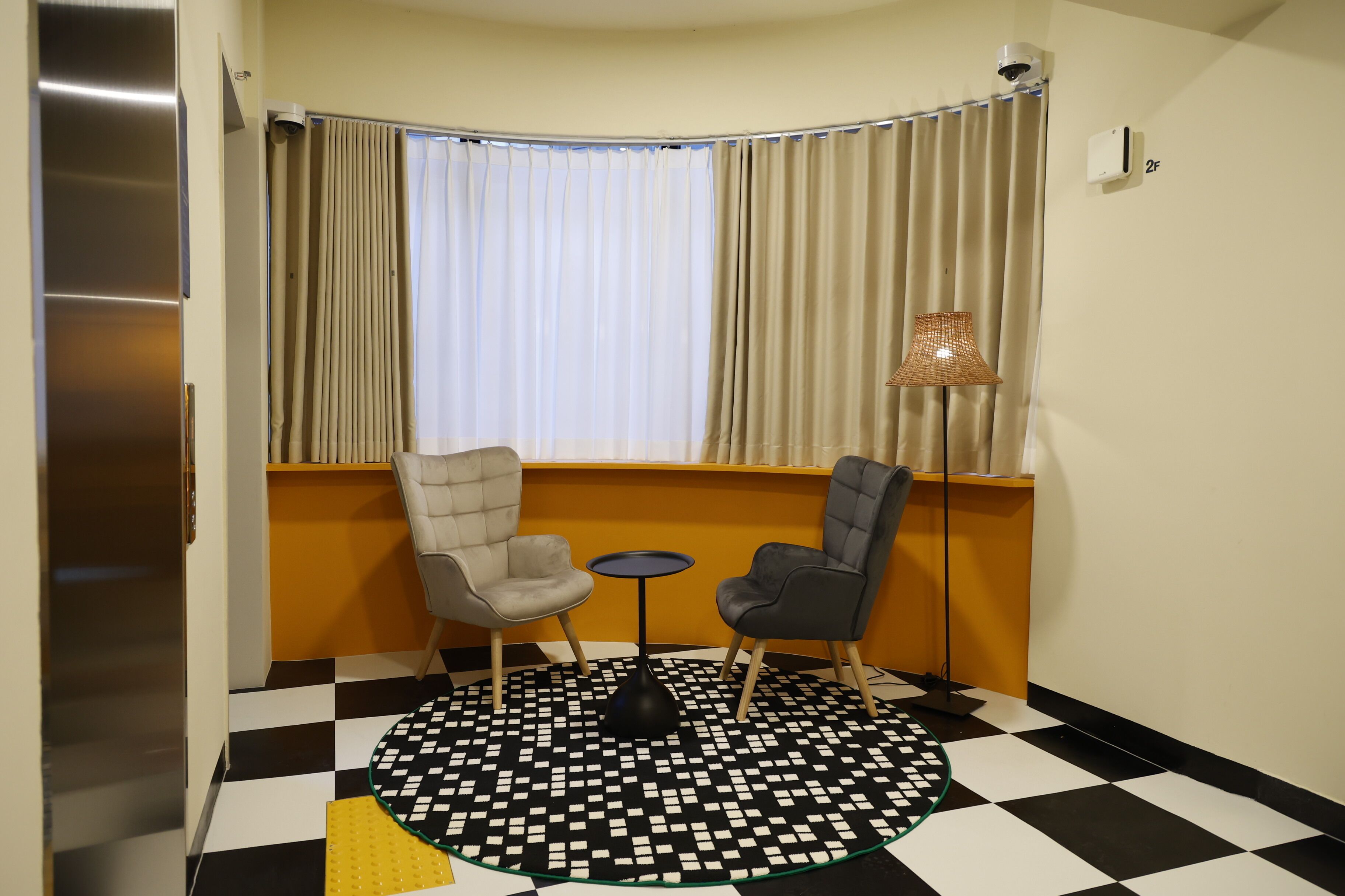 A room with a checkered floor, two chairs, a small table, and a window with curtains.