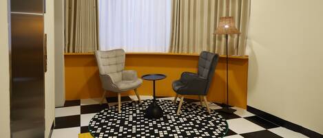 A room with a checkered floor, two chairs, a small table, and a window with curtains.