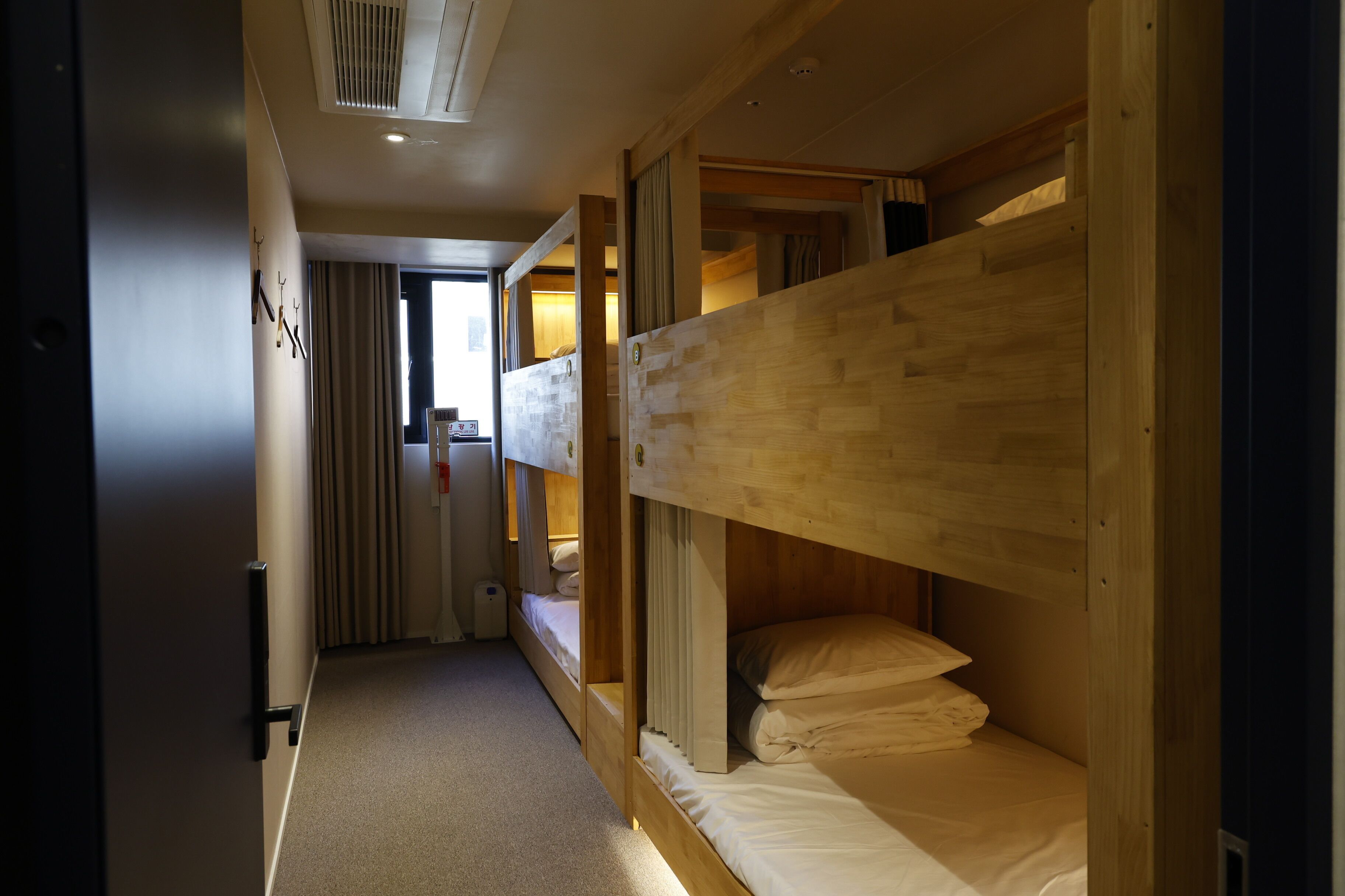 A hotel room with bunk beds, a small window, and a door leading to another room.