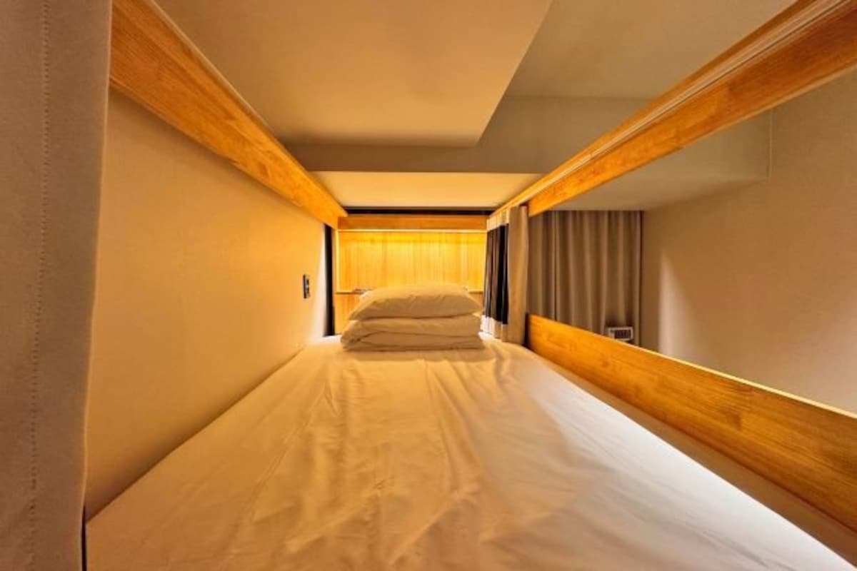 A narrow hallway leading to a room with a bed, wooden paneling, and a window with curtains.