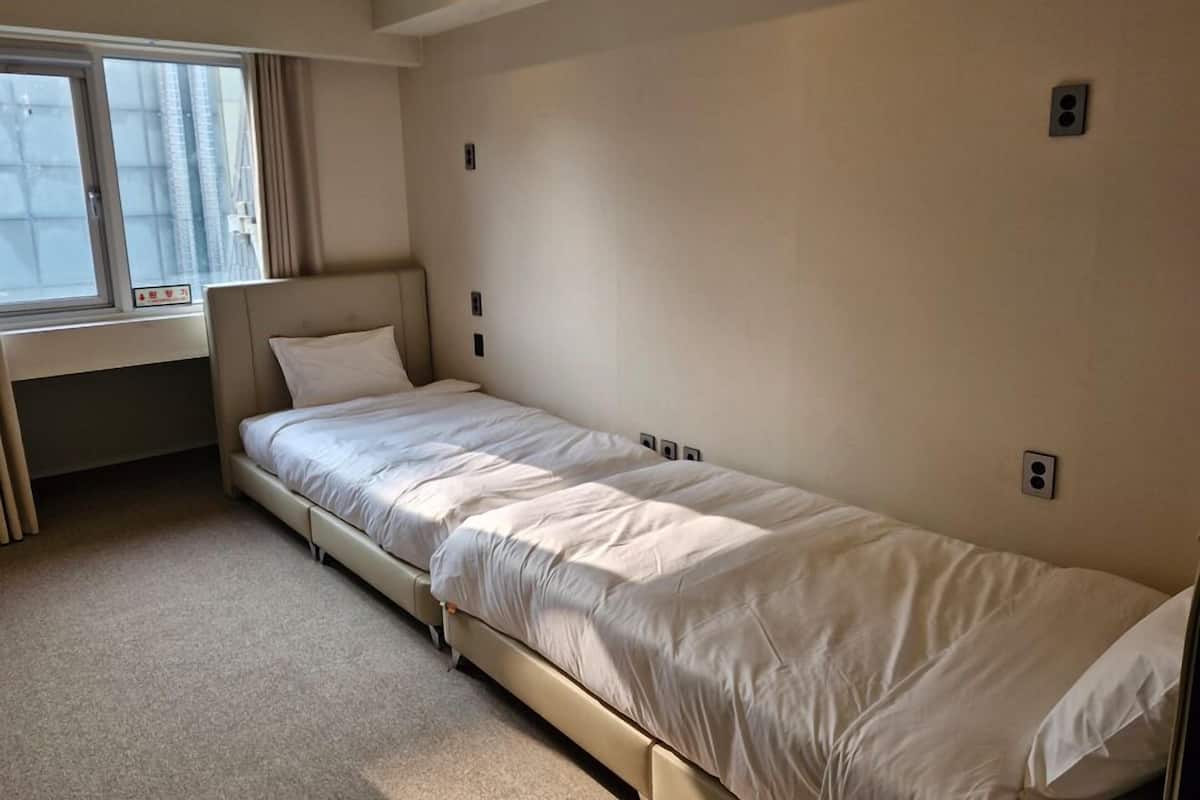 Een eenpersoonsbed in een kamer met een raam, een bureau en een stoel.