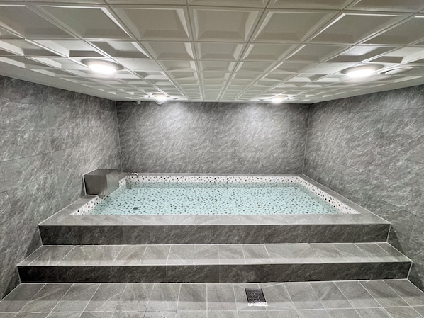 Ein Wellnessbereich mit einem rechteckigen Whirlpool, Treppen und einer Decke mit Einbauleuchten.