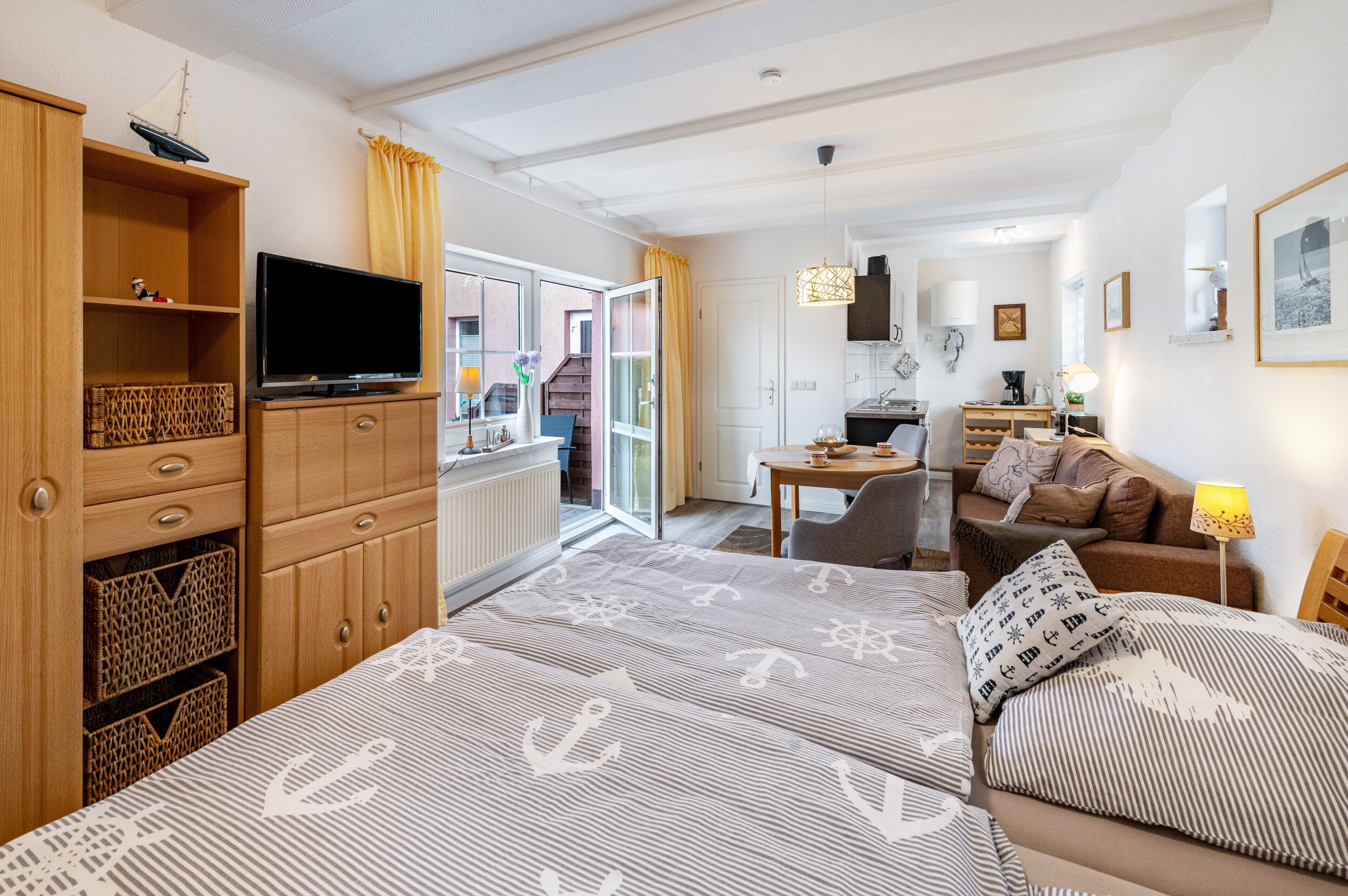 A hotel room with a bed, a TV, wooden furniture, a kitchen area, and a view of the outside.