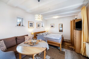 Quarto de hotel com sofá, cama, mesa com bandeja, televisão e quadros nas paredes.