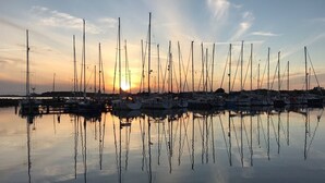 Ein Yachthafen mit mehreren Segelbooten, die im ruhigen Wasser spiegeln, und ein Sonnenuntergang im Hintergrund.