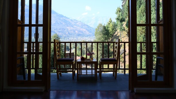 A wooden balcony with two chairs and a table, overlooking a mountainous landscape.