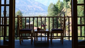 An open balcony with wooden railings, two chairs, and a table with a vase of flowers.