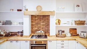 Eine Küche mit weißen Schränken, einer Ziegelrückwand, einer Holz Arbeitsplatte und verschiedenen Küchengeräten.