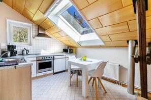 Una cocina moderna con tragaluces, armarios blancos, una mesa de comedor con sillas y vistas a árboles a través del tragaluz.