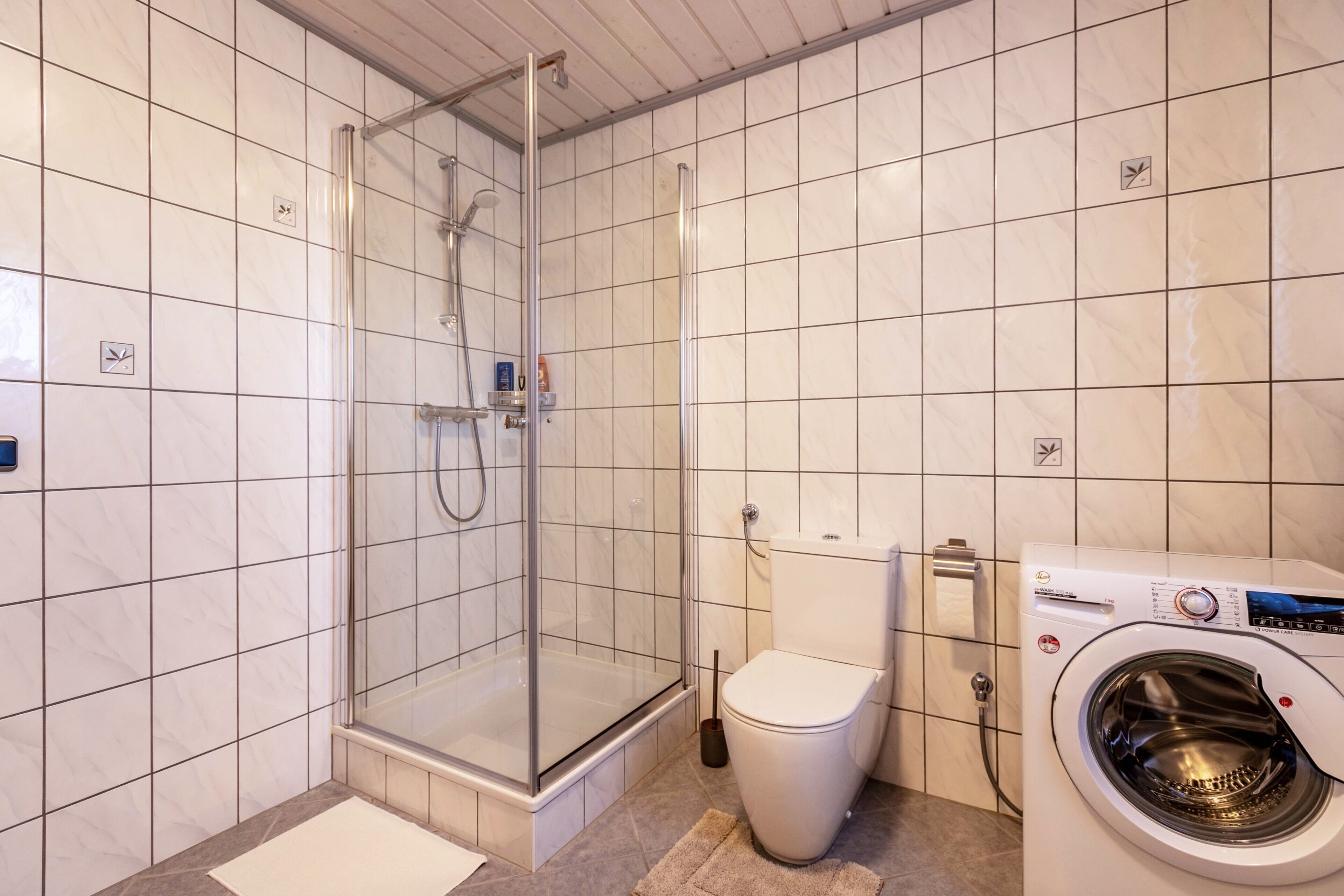 A bathroom with a glass-enclosed shower, a toilet, and a washing machine.