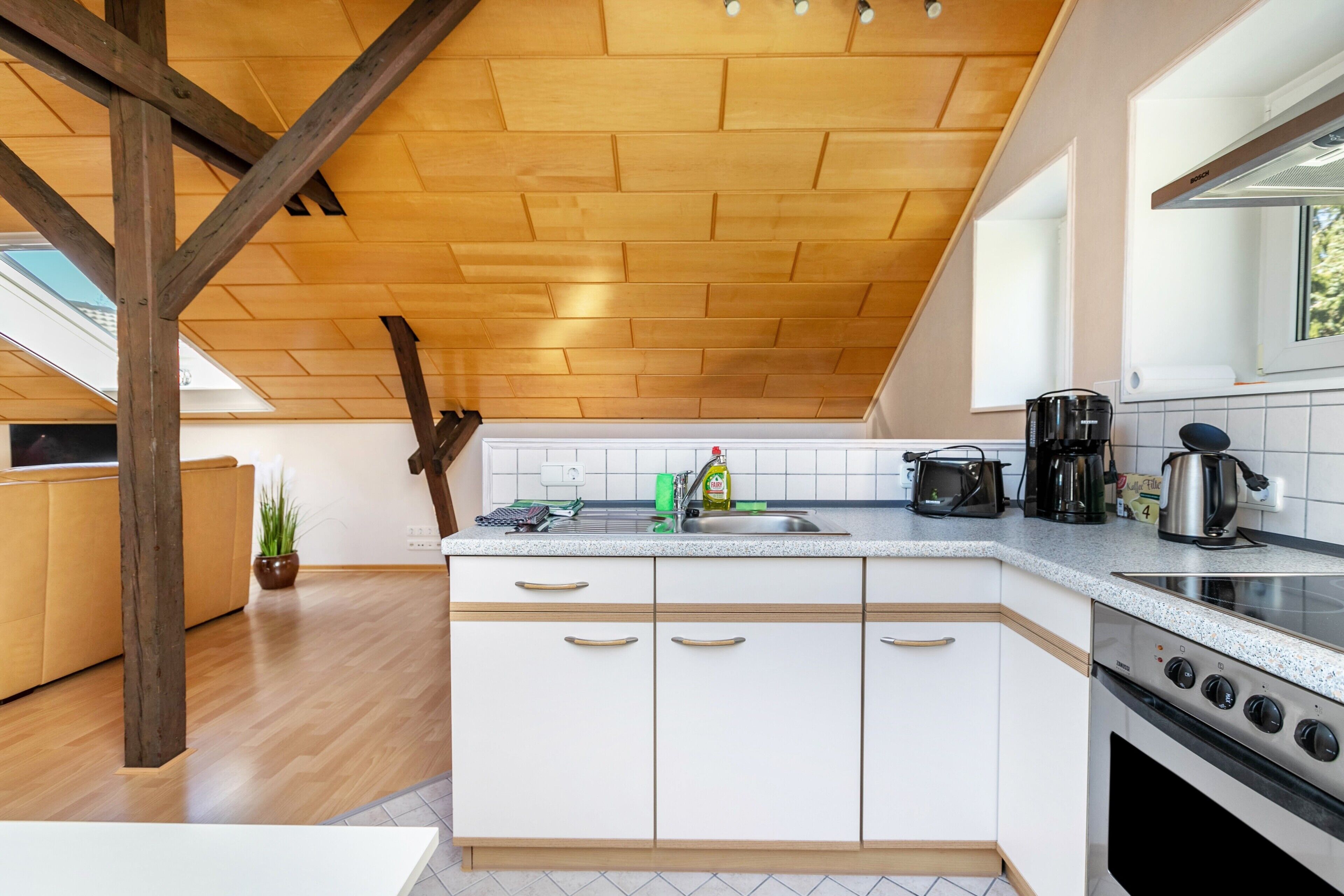 A modern kitchen with wooden beams, a large island, white cabinets, and a stove.