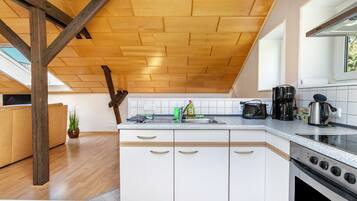 A modern kitchen with wooden beams, a large island, white cabinets, and a stove.