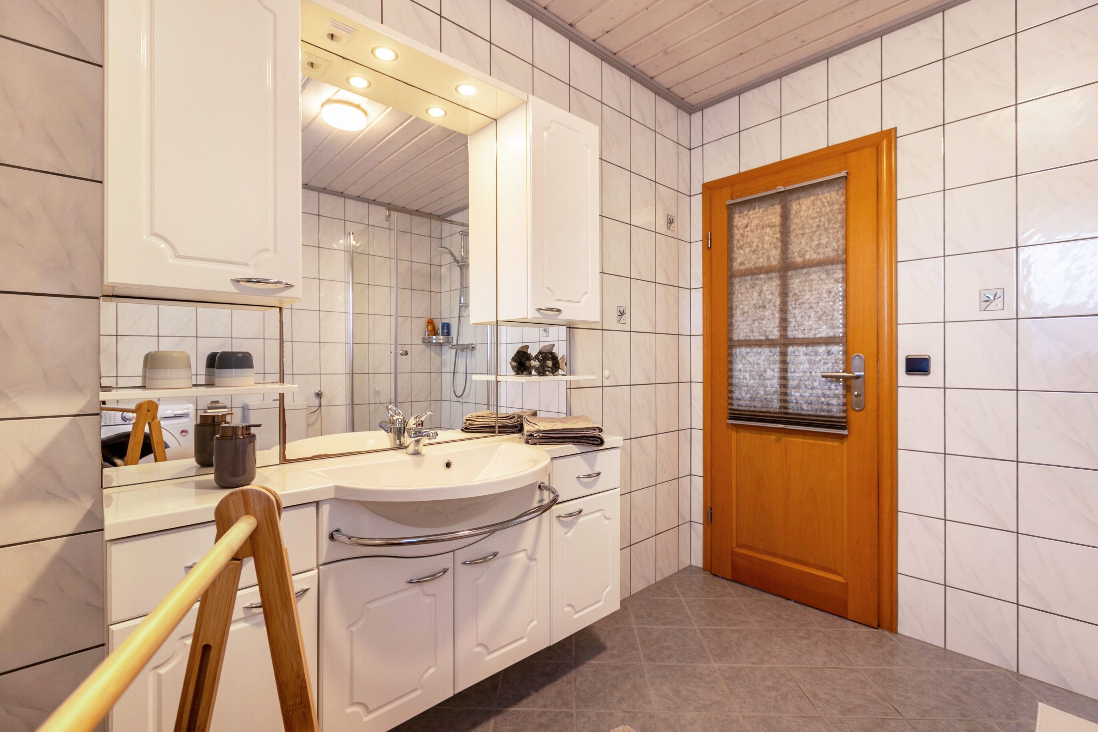 A bathroom with a sink, mirror, cabinets, and a shower.
