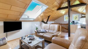 A modern loft-style living space with a sloped ceiling, a flat-screen TV, leather sofas, a wooden coffee table, and a kitchen area in the background. - Studio 'Alte Schmiede' with Wi-Fi and Air Conditioning (Kuden)