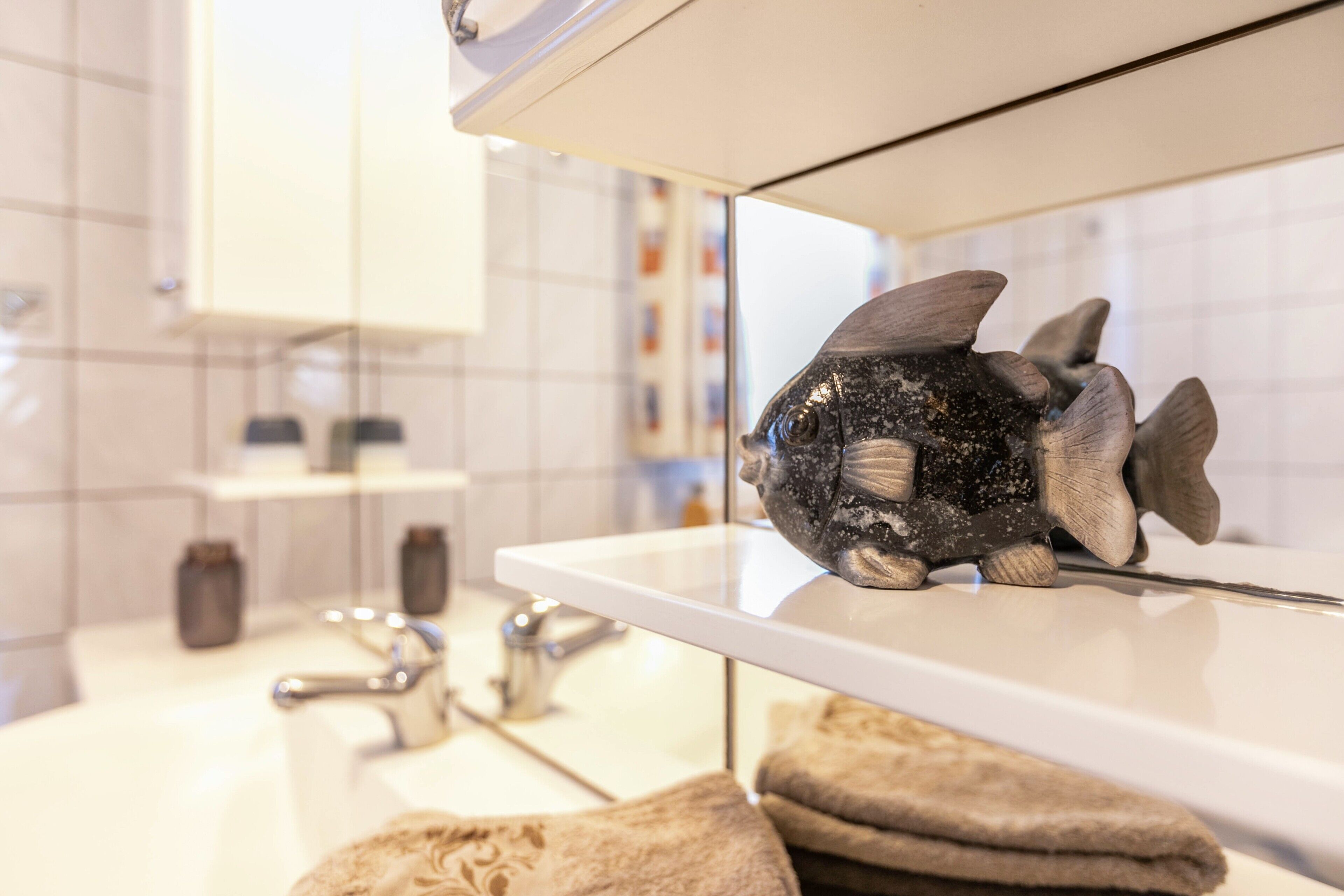 A bathroom with a white sink, a mirror, and a decorative fish on the edge of the sink.