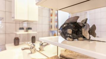 A bathroom with a white sink, a mirror, and a decorative fish on the edge of the sink.