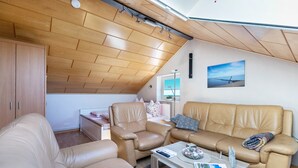A modern living room with a wooden ceiling, a tan leather sofa, a leather armchair, and a coffee table with remote controls and magazines. - Studio 'Alte Schmiede' with Wi-Fi and Air Conditioning (Kuden)