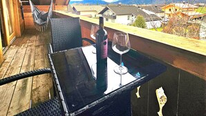Eine Holzterrasse mit einem Glastisch, zwei Korbstühlen, einer Weinflasche und einem Weinglas.