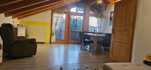 A cozy room with a wooden ceiling, a dining area with a table and chairs, and a large window with curtains.