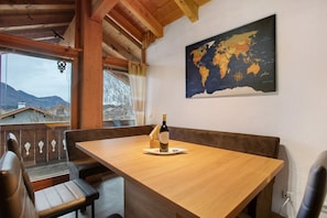 Une table en bois avec une bouteille et des verres, une carte du monde accrochée au mur et, par la fenêtre, une vue sur les montagnes.