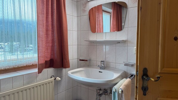 A bathroom with a white sink, a mirror, and a window with a curtain. - Apartment '1' with Mountain View, Shared Terrace and Wi-Fi (Leutasch)