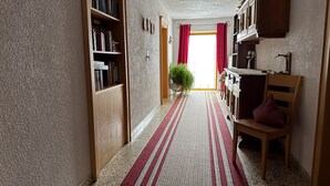 A hallway with a patterned carpet, wooden bookshelves, a wooden chair, and a potted plant. - Apartment '1' with Mountain View, Shared Terrace and Wi-Fi (Leutasch)