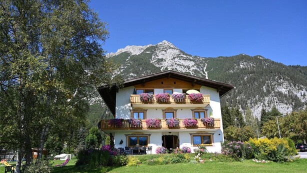 A multi-story hotel with balconies adorned with flowers, set against a backdrop of mountains. - Apartment '1' with Mountain View, Shared Terrace and Wi-Fi (Leutasch)