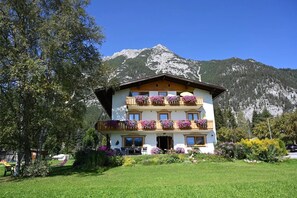 A multi-story hotel with balconies adorned with flowers, set against a backdrop of mountains. - Apartment '1' with Mountain View, Shared Terrace and Wi-Fi (Leutasch)