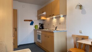A compact kitchen with wooden cabinets, a built-in oven, a sink, and a small dining area with a chair. - Studio Apartment '3' with Mountain View, Shared Terrace and Wi-Fi (Leutasch)