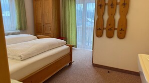A bedroom with a wooden bed, a radiator, a window with curtains, and a wall-mounted ski rack. - Studio Apartment '3' with Mountain View, Shared Terrace and Wi-Fi (Leutasch)