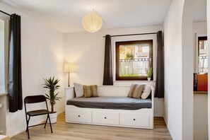 A compact room with a bed, a chair, a potted plant, a window with curtains, and a hanging light fixture. - Apartment 'Weinberg' with Balcony and Wi-Fi (Zeilarn)