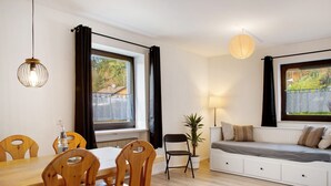 Een kamer met een houten eettafel, stoelen, een bank, een potplant en een raam met gordijnen.