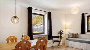 Een kamer met een eettafel, stoelen, een bank, een lamp en een hanglamp.
