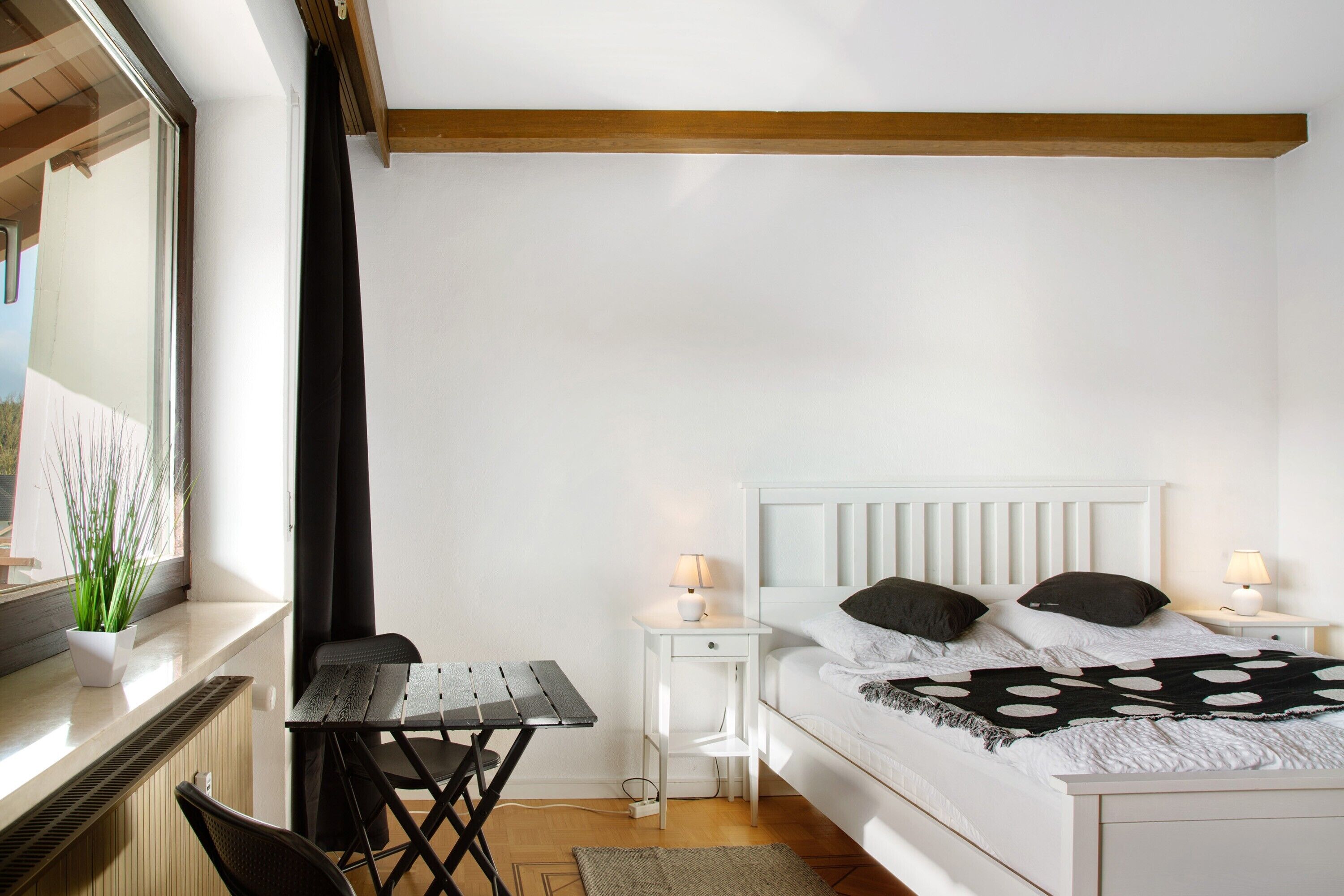 A bedroom with a bed, bedside tables, a desk, and a window with a plant.