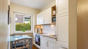 A compact kitchen with white cabinets, a glass table, and a window with a view of greenery. - Apartment 'Westerdeich' with Private Terrace, Shared Garden and Wi-Fi (Westerdeichstrich)