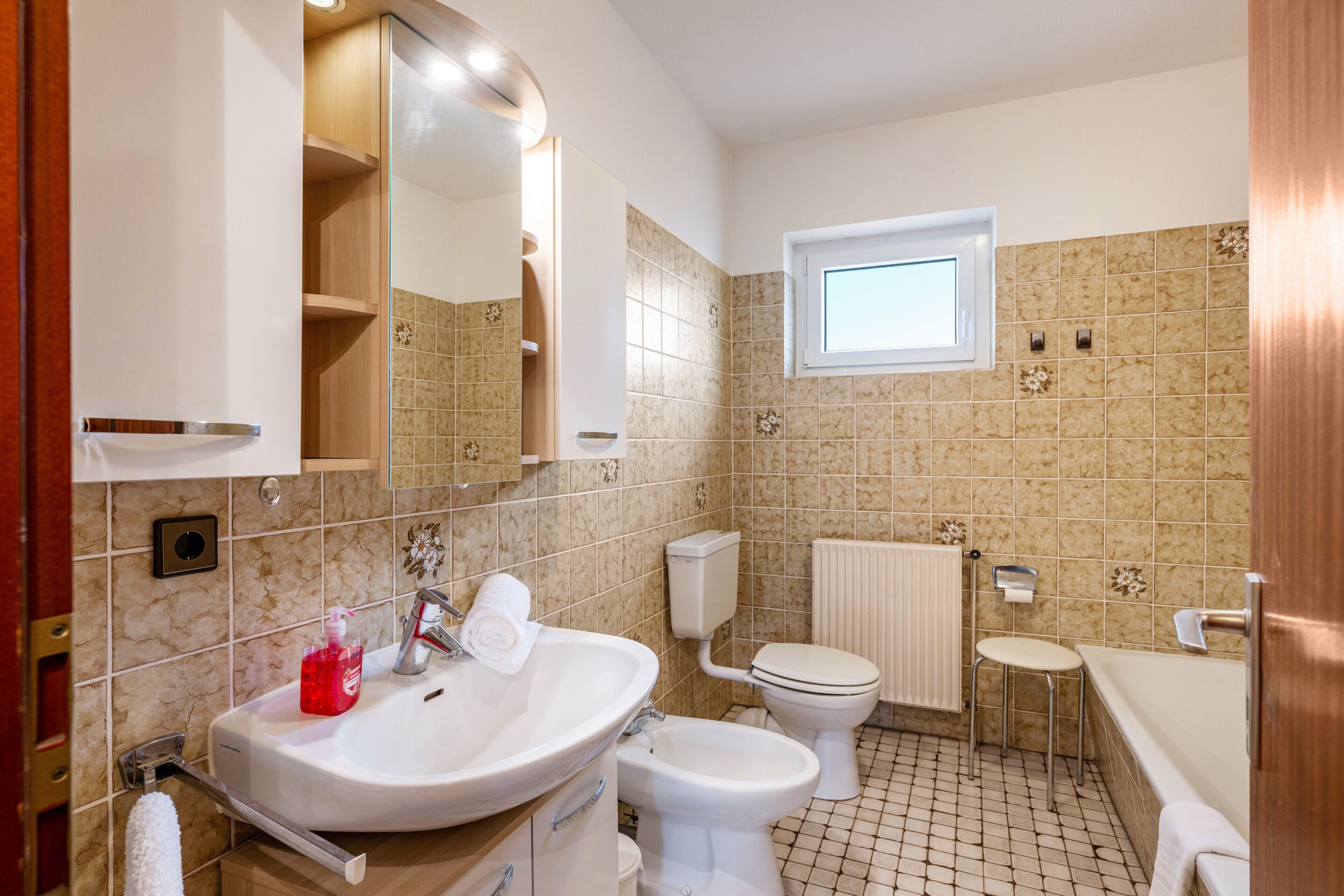 A bathroom with a sink, toilet, bidet, and a small window.