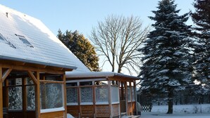A snow-covered building with a wooden structure, a glass enclosure, and a snow-covered tree in the background. - Apartment 'Am Graben' with Private Terrace, Shared Garden and Wi-Fi (Westerdeichstrich)
