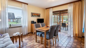 A dining area with a wooden table and chairs, a television, and a view of the outside. - Apartment 'Am Graben' with Private Terrace, Shared Garden and Wi-Fi (Westerdeichstrich)