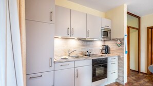 A compact kitchen with white cabinets, a microwave, a stove, and a sink. - Apartment 'Am Graben' with Private Terrace, Shared Garden and Wi-Fi (Westerdeichstrich)