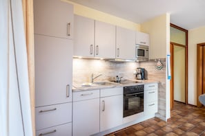 Une cuisine de taille réduite, avec des meubles blancs, un four à micro-ondes, une cuisinière et un évier.