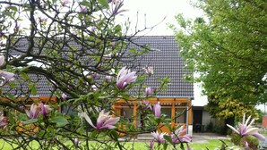 A garden with blooming magnolia trees and a building with a tiled roof. - Apartment 'Am Graben' with Private Terrace, Shared Garden and Wi-Fi (Westerdeichstrich)